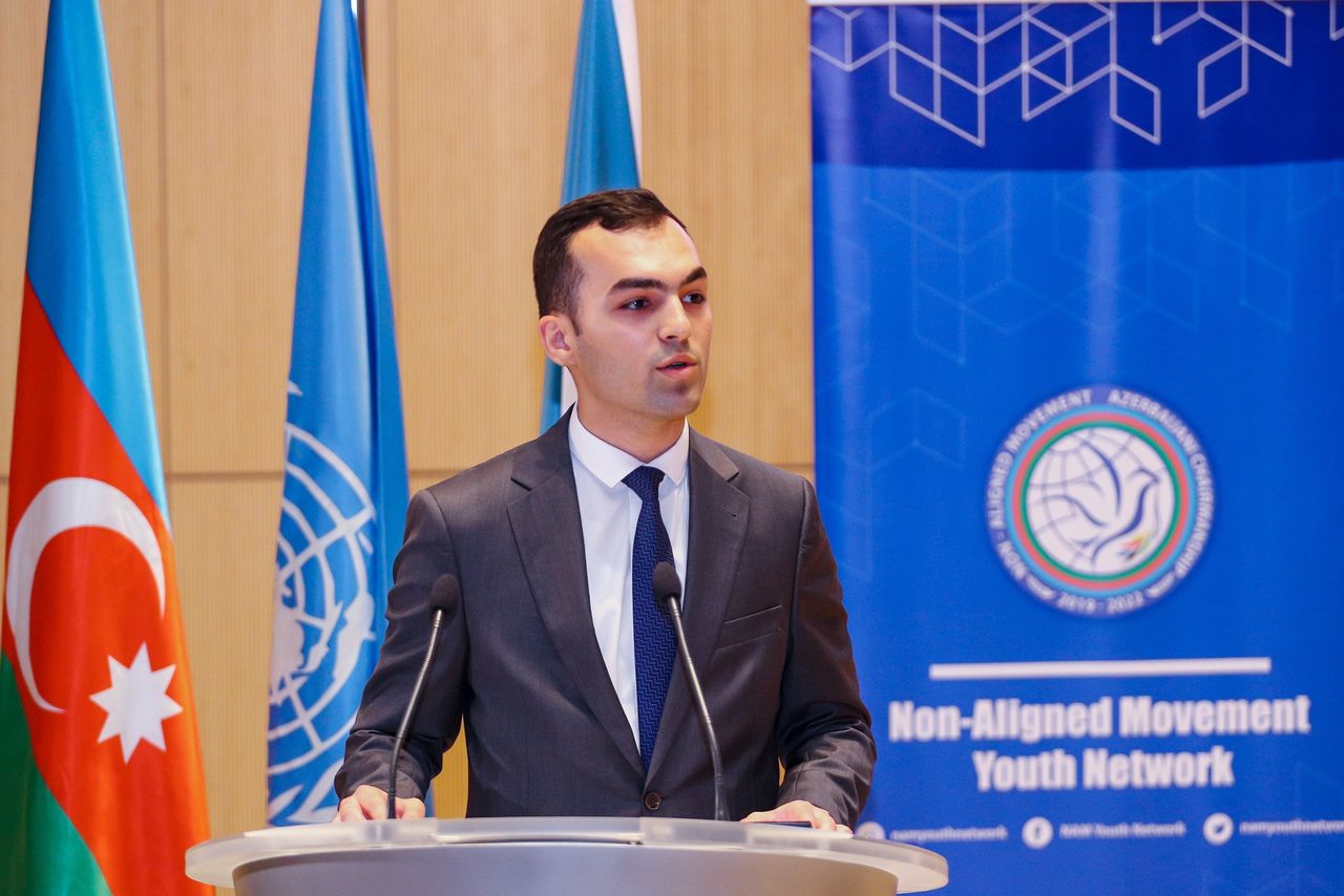 Ordukhan Gahramanzada speaking at a lectern between the flags of Azerbaijan and the United Nations
