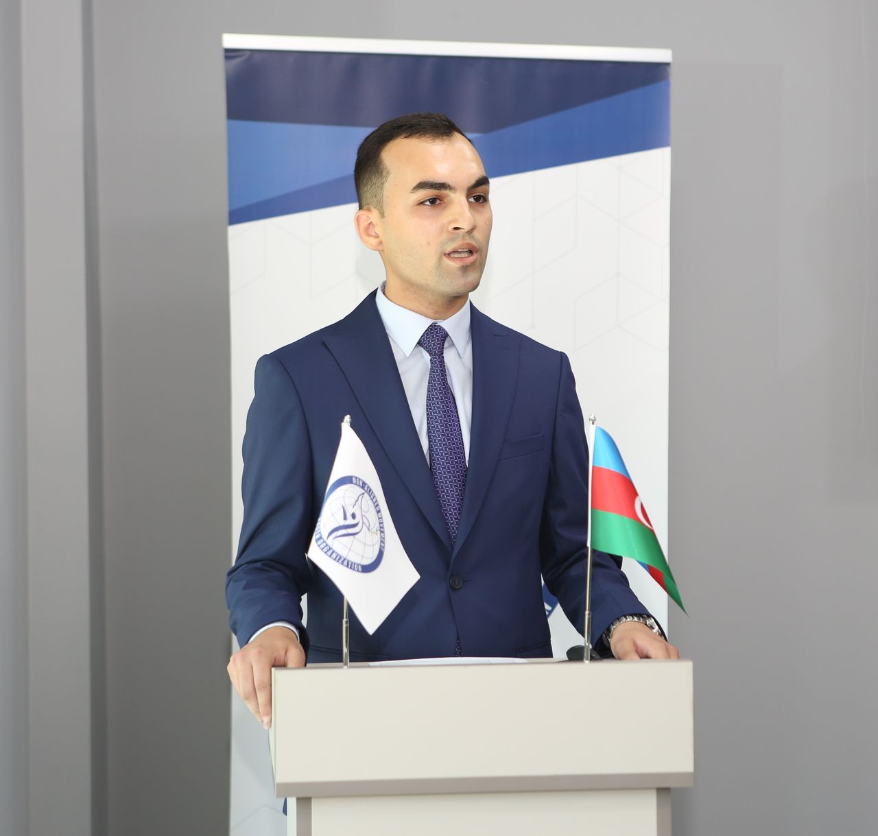 Ordukhan Gahramanzada speaking at a lectern beside the flag of Azerbaijan